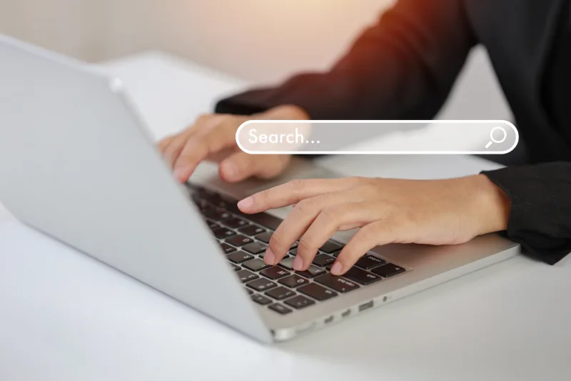 191945770_l A person typing on a silver laptop with a digital search bar graphic floating over the keyboard area.