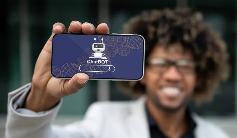 209074148_l A person holding a smartphone displaying a ChatBOT logo against a blurred background, emphasizing technology and communication.