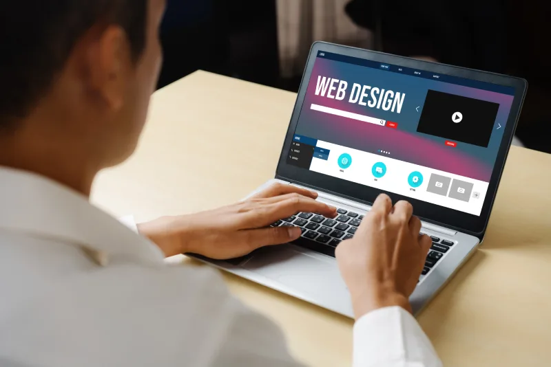 247446278_l A person using a laptop on a desk, focused on a web design interface with video and editing tools displayed on the screen.
